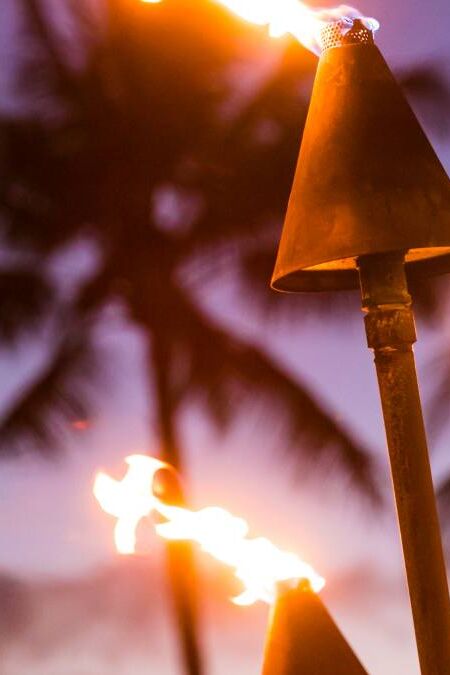 Hawaii sunset with lit tiki torches. Hawaiian icon, lights burning at dusk at beach resort or restaurants for outdoor lighting and decoration, cozy atmosphere.