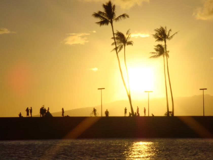 Beautiful sunset picture with silhouette of many people doing different activity, at Magic Island Lagoon in the city of Honolulu, Oahu