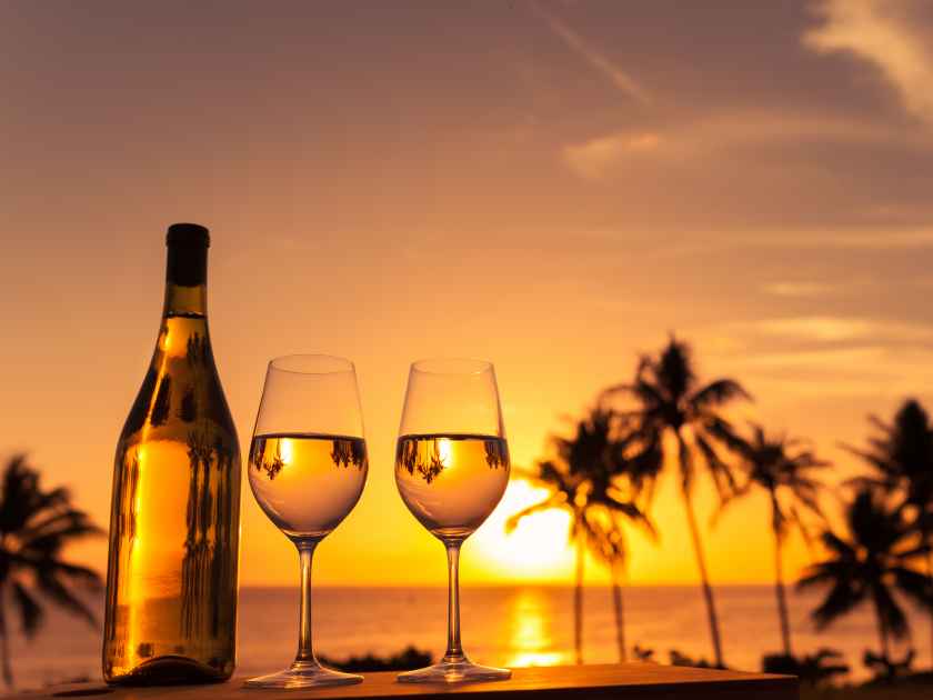 Romantic glass of wine setting by the beach against a colorful sunset.