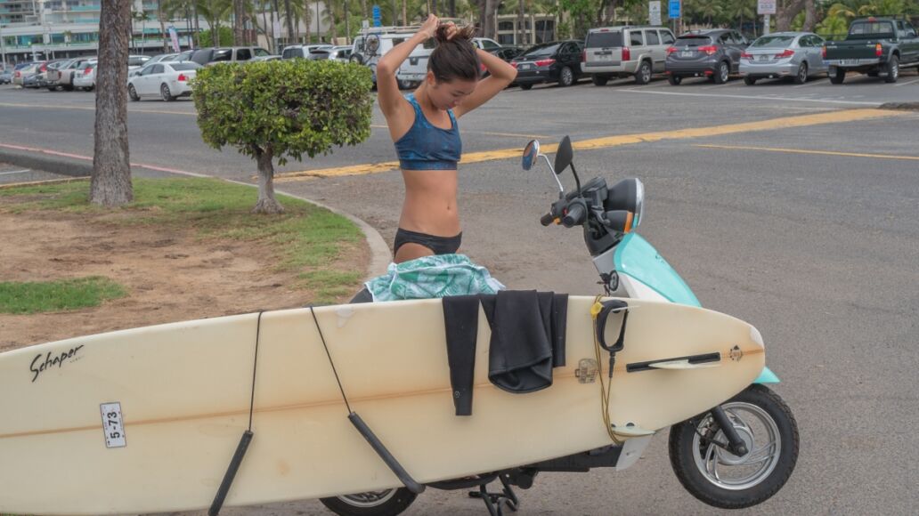 Honolulu, Hawaii, USA, Nov. 28, 2017. Young Hawaiian surfer girl with her surfboard loaded on her scooter for the trip home after a morning of surfing.