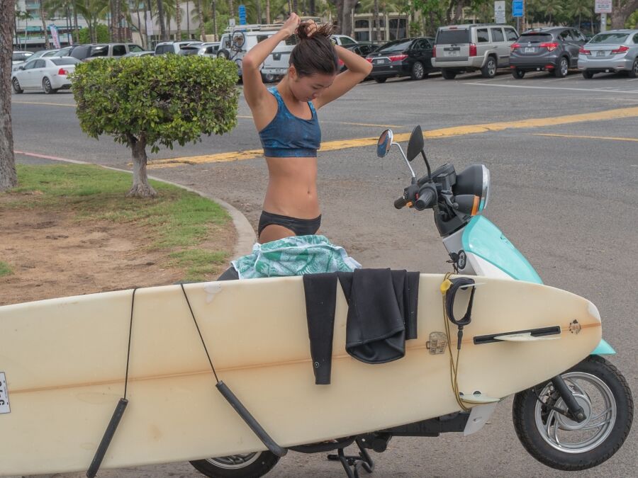 Honolulu, Hawaii, USA, Nov. 28, 2017. Young Hawaiian surfer girl with her surfboard loaded on her scooter for the trip home after a morning of surfing.