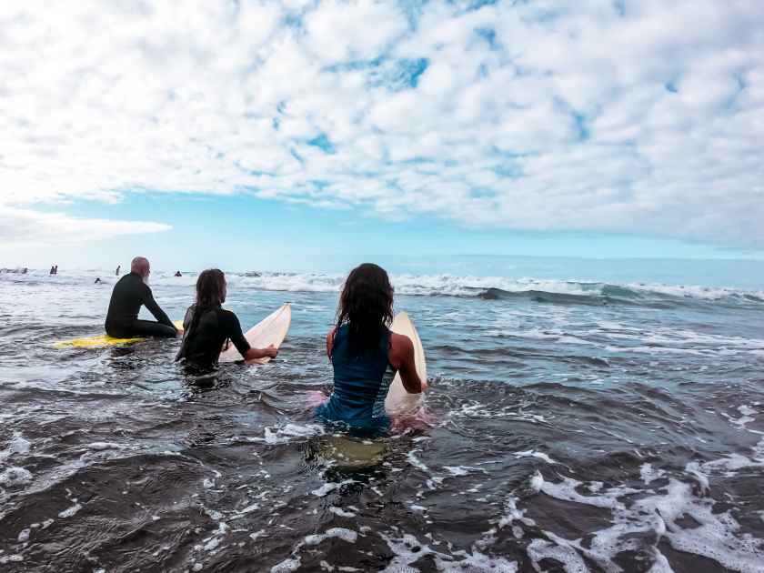 Happy family having fun surfing in the morning. Surfers father, son and girlfriend waiting for a wave of the ocean. Sporty people lifestyle and extreme sport concept