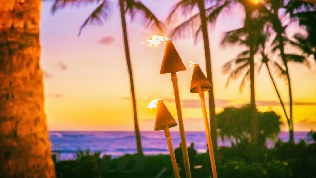 Hawaii luau party with fire torches at sunset. Hawaiian icon, lights burning at dusk at Waikiki beach resort restaurant for outdoor lighting cozy atmosphere.