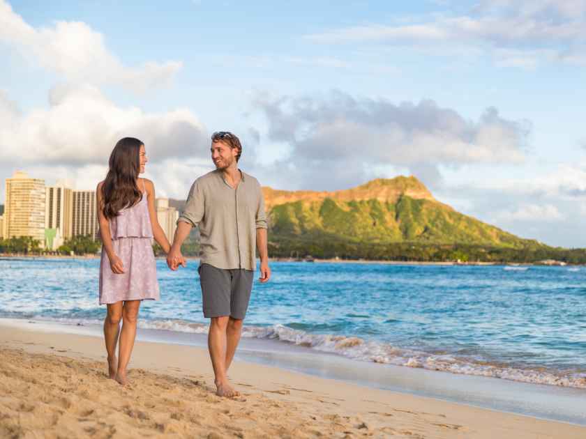 Couple walking on Waikiki beach Hawaii vacation. Happy couple in love relaxing at sunset on tourist famous travel destination in Honolulu, Oahu, Hawaii.