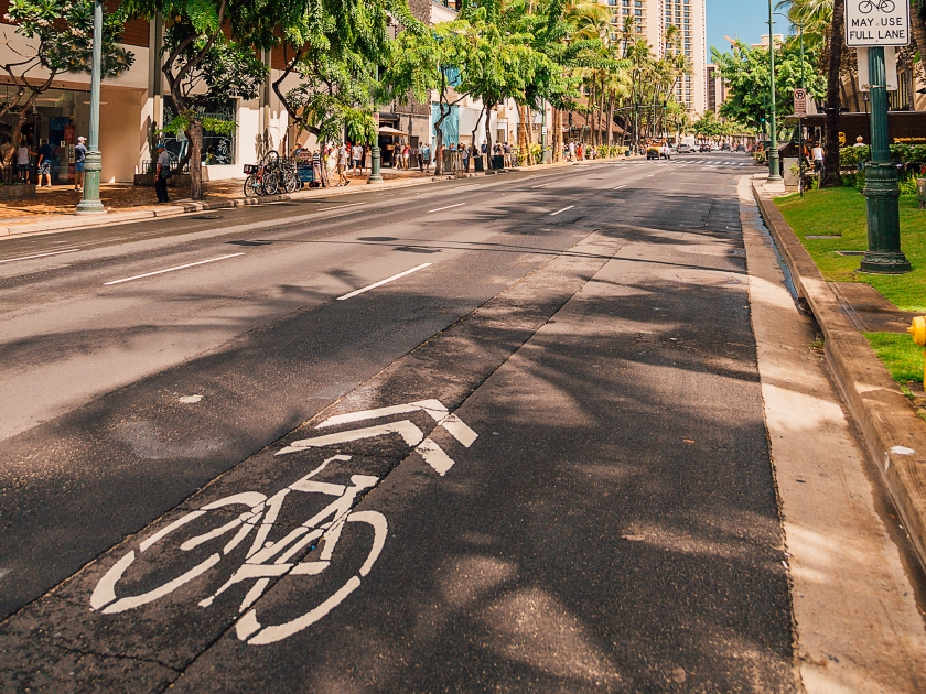 Beautiful sunny street of Honolulu, Hawaii with many plants, bike lane and traffic lights.