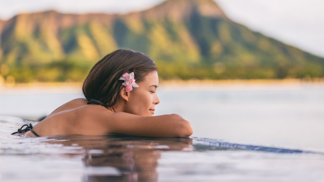 Luxury resort wellness pampering spa lifestyle Asian woman relaxing in infinity swimming pool of outdoor hotel on Waikiki beach, Honolulu, Hawaii travel.