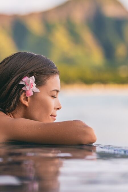 Luxury resort wellness pampering spa lifestyle Asian woman relaxing in infinity swimming pool of outdoor hotel on Waikiki beach, Honolulu, Hawaii travel.