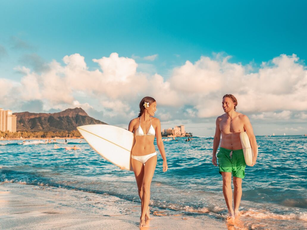 Hawaii Honolulu couple surfers happy on waikiki beach with surfboards. Healthy active sport lifestyle fitness people at sunset with diamond head mountain landscape.