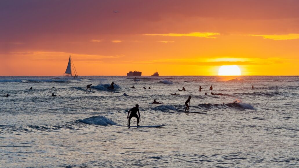 View from Waikiki beach at beautiful sunset with silhouettes of swimmers and surfers, Honolulu, Oahu, Hawaii, USA