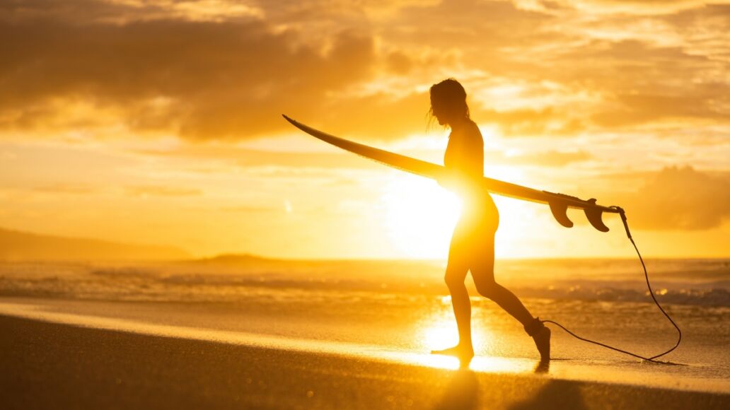 A silhouette of a girl surfer on the beach at sunset. A woman walking from the ocean after surf on banzai pipeline north shore Oahu Hawaii.