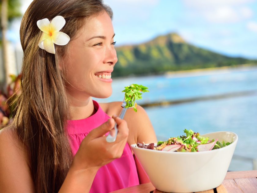 Salad eating healthy woman at restaurant in Hawaii. Asian Multiracial young female adult sitting at beach cafe eating a vegetarian lunch meal during summer vacations in Waikiki, Honolulu, Hawaii, USA.