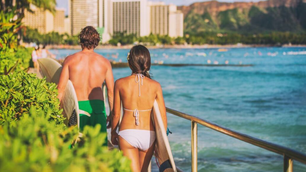 Hawaii beach surfing lifestyle. Young surfers people walking with surfboards on Waikiki beach tourists on summer travel vacations.