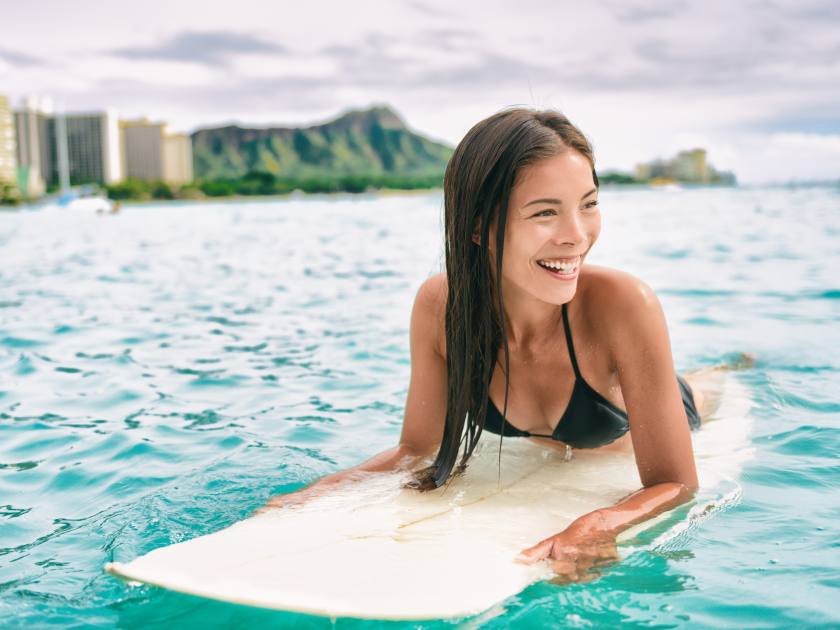 Surf class in Waikiki Hawaii - Surfing Asian surfer girl on surfbaord lesson in Hawaii paddling in ocean waves. Sexy sports athlete training in water. Watersport active lifestyle.