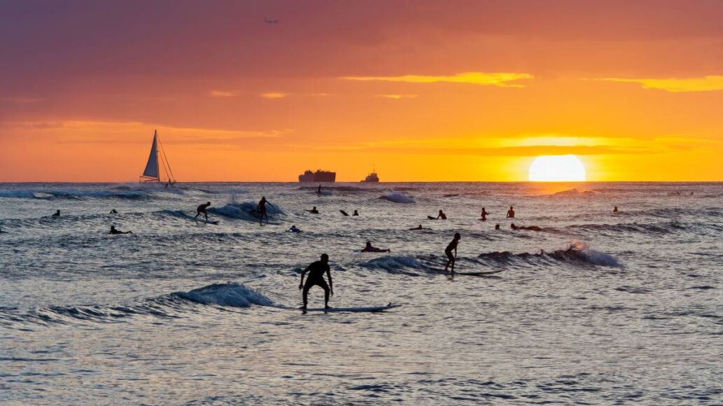 View from Waikiki beach at beautiful sunset with silhouettes of swimmers and surfers, Honolulu, Oahu, Hawaii, USA