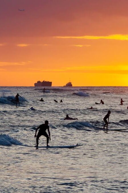 View from Waikiki beach at beautiful sunset with silhouettes of swimmers and surfers, Honolulu, Oahu, Hawaii, USA