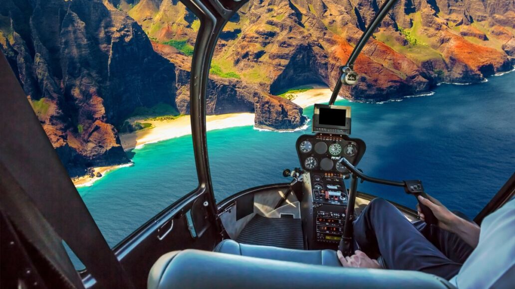 Helicopter cockpit flies in Na Pali coast, Kauai, Hawaii, United States, with pilot arm and control board inside the cabin.